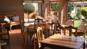 A covered outdoor seating area with wooden tables and chairs, a brick wall, and potted plants. - Siesta B&B (Abaqulusi)