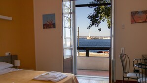 A hotel room with a bed, a chair, and a view of the sea through an open door. - Teatro sullo Stretto (Messina)