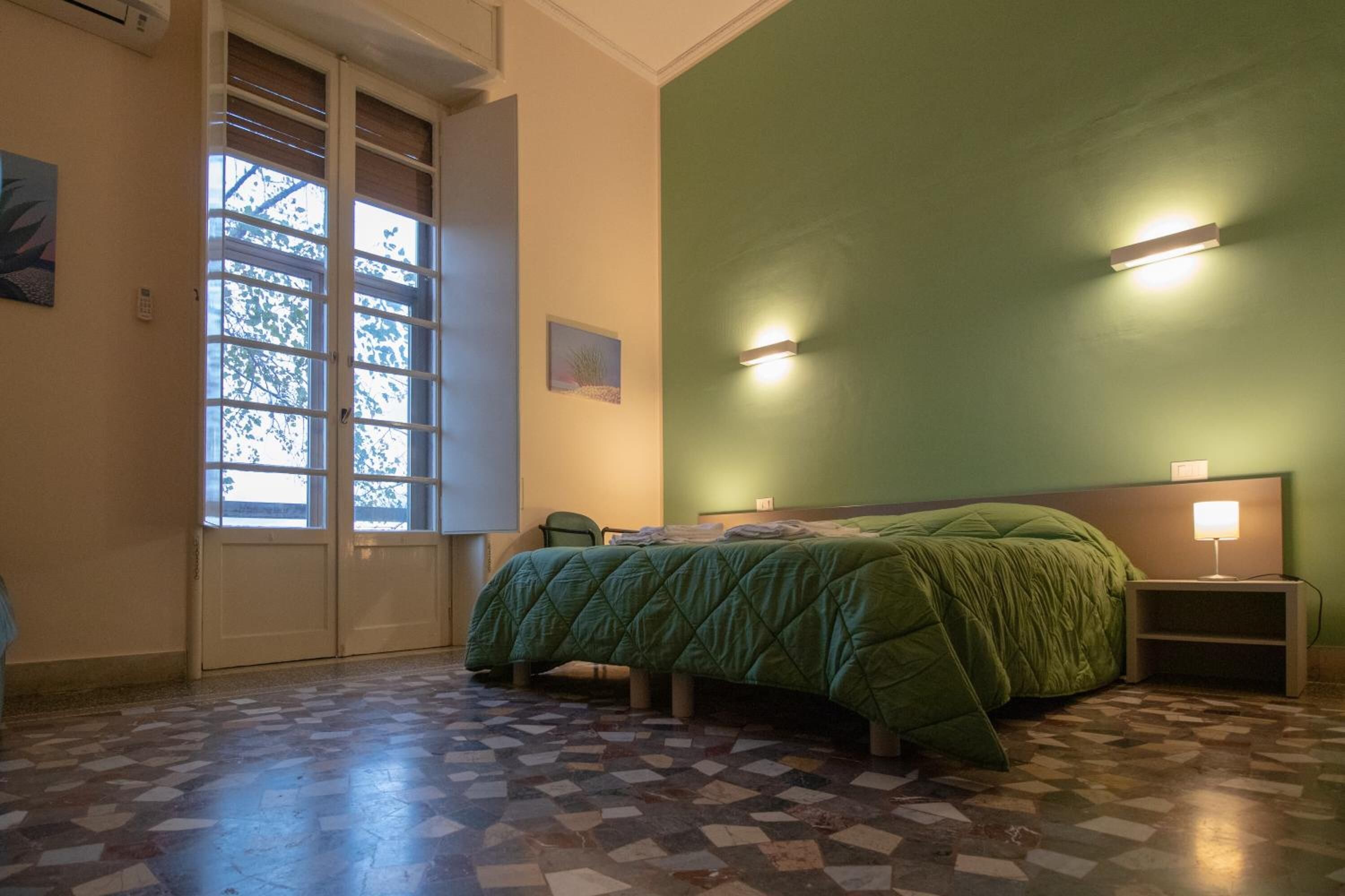 Un dormitorio con cama, mesita de noche, silla, ventana con persianas y suelo estampado.