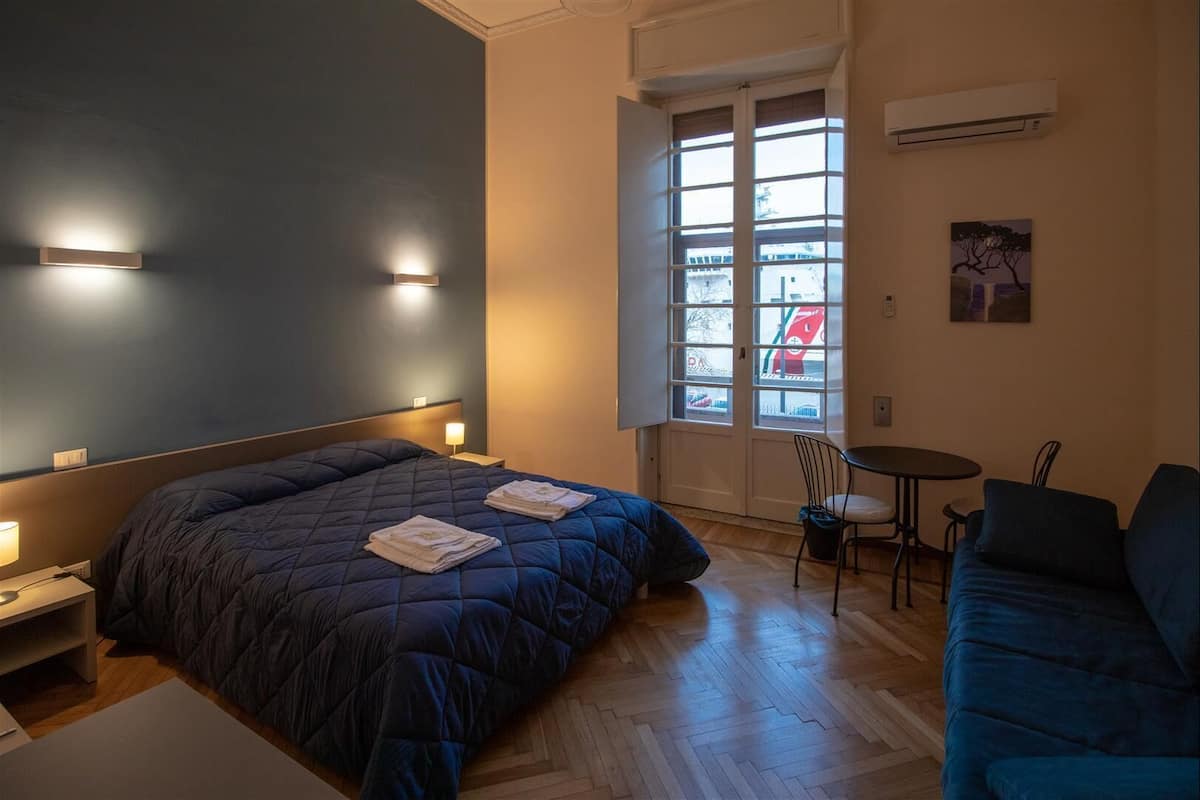 A bedroom with a bed, bedside tables, a desk, a chair, a small table, and a window with a view of the outside.