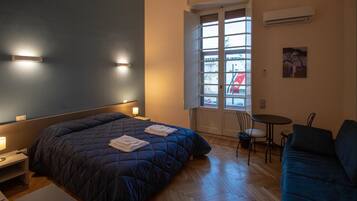 A bedroom with a bed, bedside tables, a desk, a chair, a small table, and a window with a view of the outside.