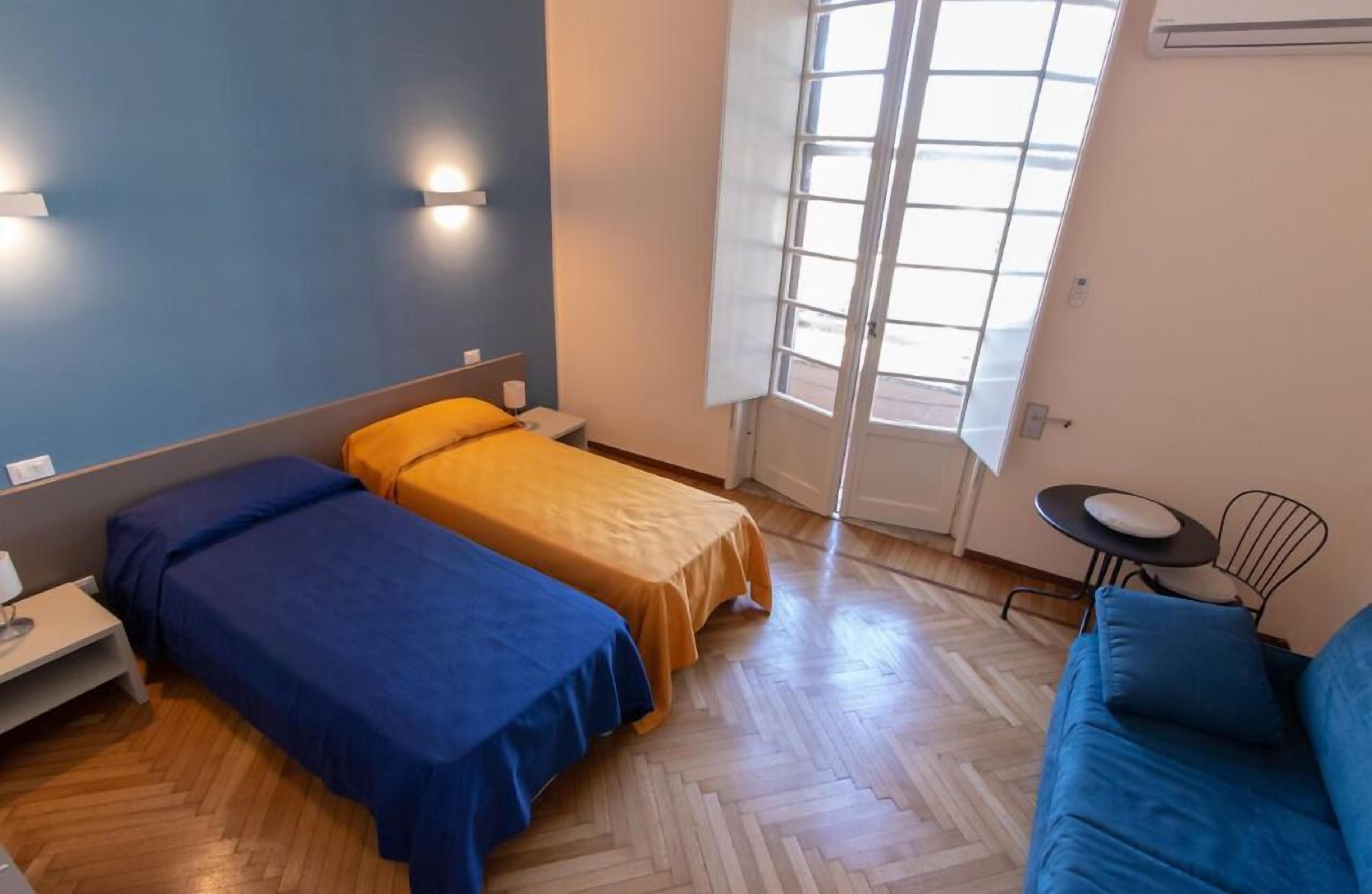 Une chambre avec deux lits, un canapé, une petite table et une fenêtre avec des stores.