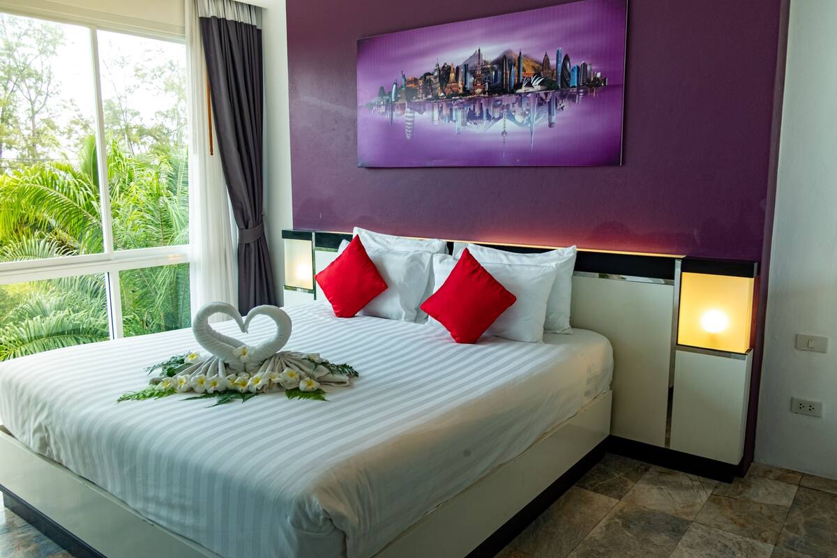 A hotel room with a bed, a heart-shaped decoration, and a cityscape painting on the wall.