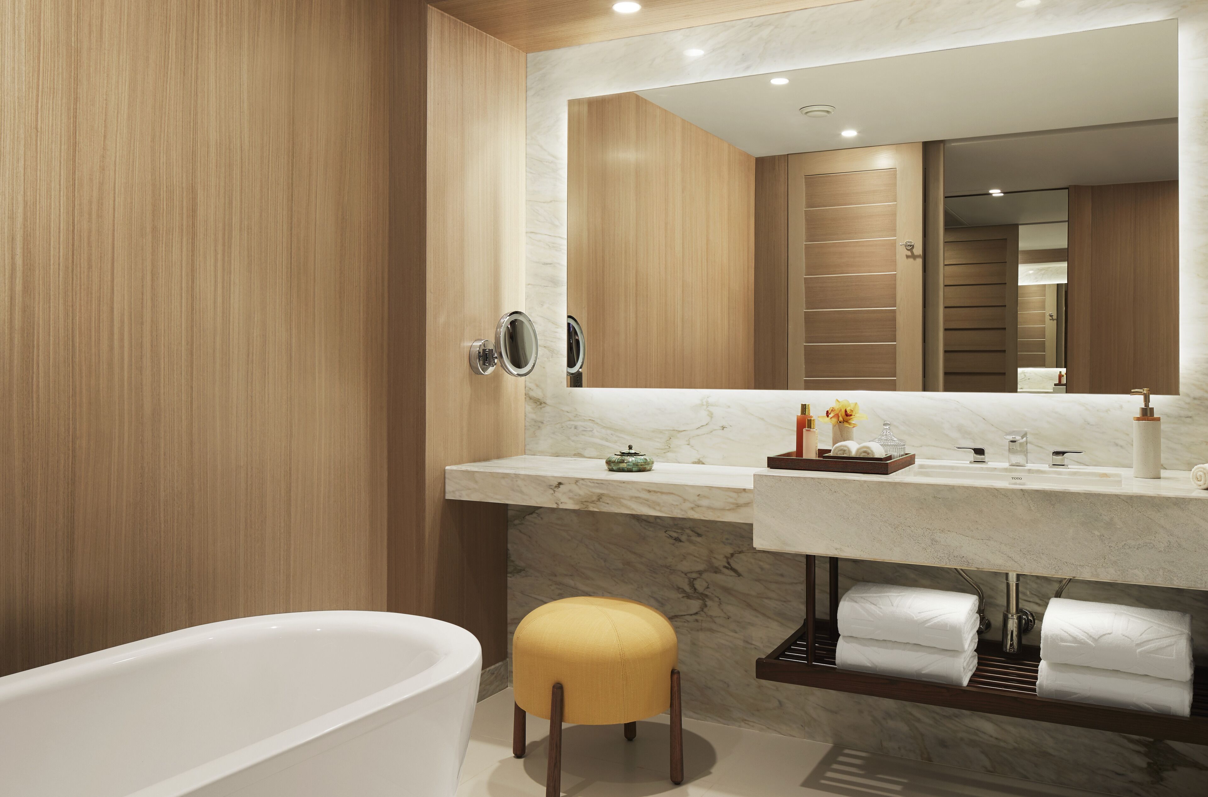 A modern bathroom with a marble vanity, a freestanding bathtub, and a wooden vanity cabinet.