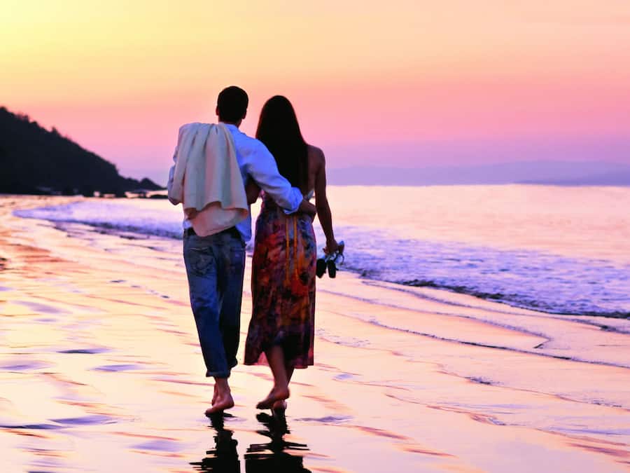 Una pareja caminando por la playa al atardecer.