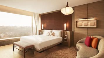 Una habitación de hotel moderna con una cama grande, mesitas de noche, un banco, un sofá y vistas a la ciudad.