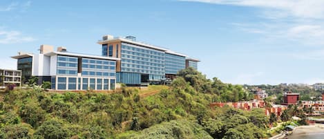 A modern hotel with a glass facade, situated on a hillside overlooking a beach.
