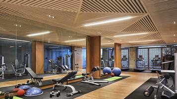 A modern gym with various exercise equipment, large mirrors, and a wooden ceiling.