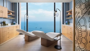 A modern room with a large window overlooking the sea, featuring two reclining chairs, wooden cabinets, and a floor lamp. - Taj Cidade de Goa Horizon, Goa (Panaji)