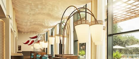 A modern restaurant with high ceilings, large windows, and a variety of seating arrangements.