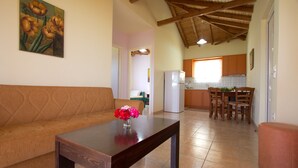 A living room with a sofa, a coffee table with flowers, a dining area with chairs and a table, and a kitchen in the background. - DIMITRA (no 4)... vacation villa in Koroni of Messinia with sea view!!! (Koroni)