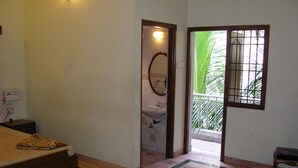 A room with a bed, a small table, a bathroom with a sink, and a window with a view of palm trees. - Lloyds Guest House , Krishna street , T. Nagar (Chennai)