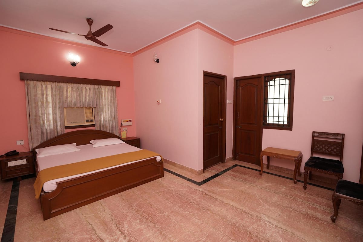 A bedroom with a bed, a ceiling fan, a window with bars, a bench, and a door.