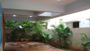 A covered outdoor area with a patterned floor, surrounded by greenery and a low wall. - Lloyds Guest House , Krishna street , T. Nagar (Chennai)