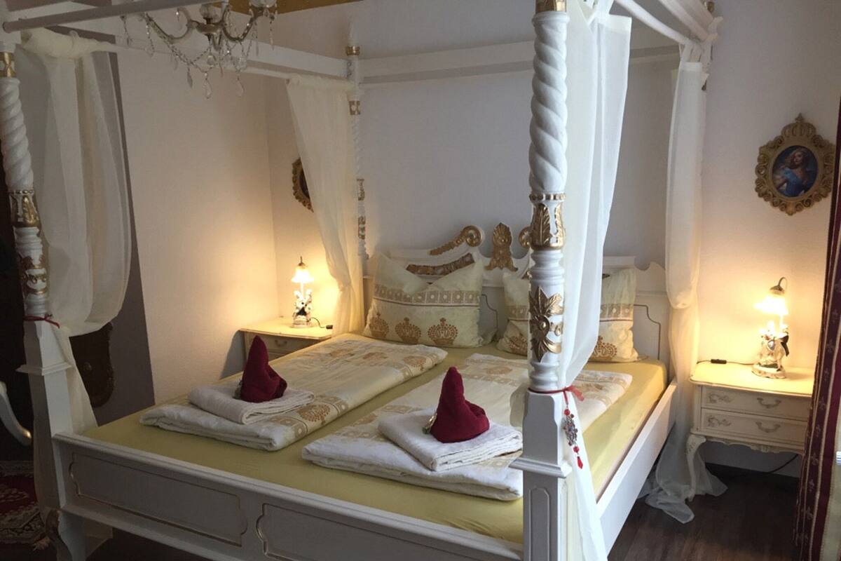 A four-poster canopy bed with two bedside tables, each with a lamp, in a room with a wooden floor and a framed picture on the wall.