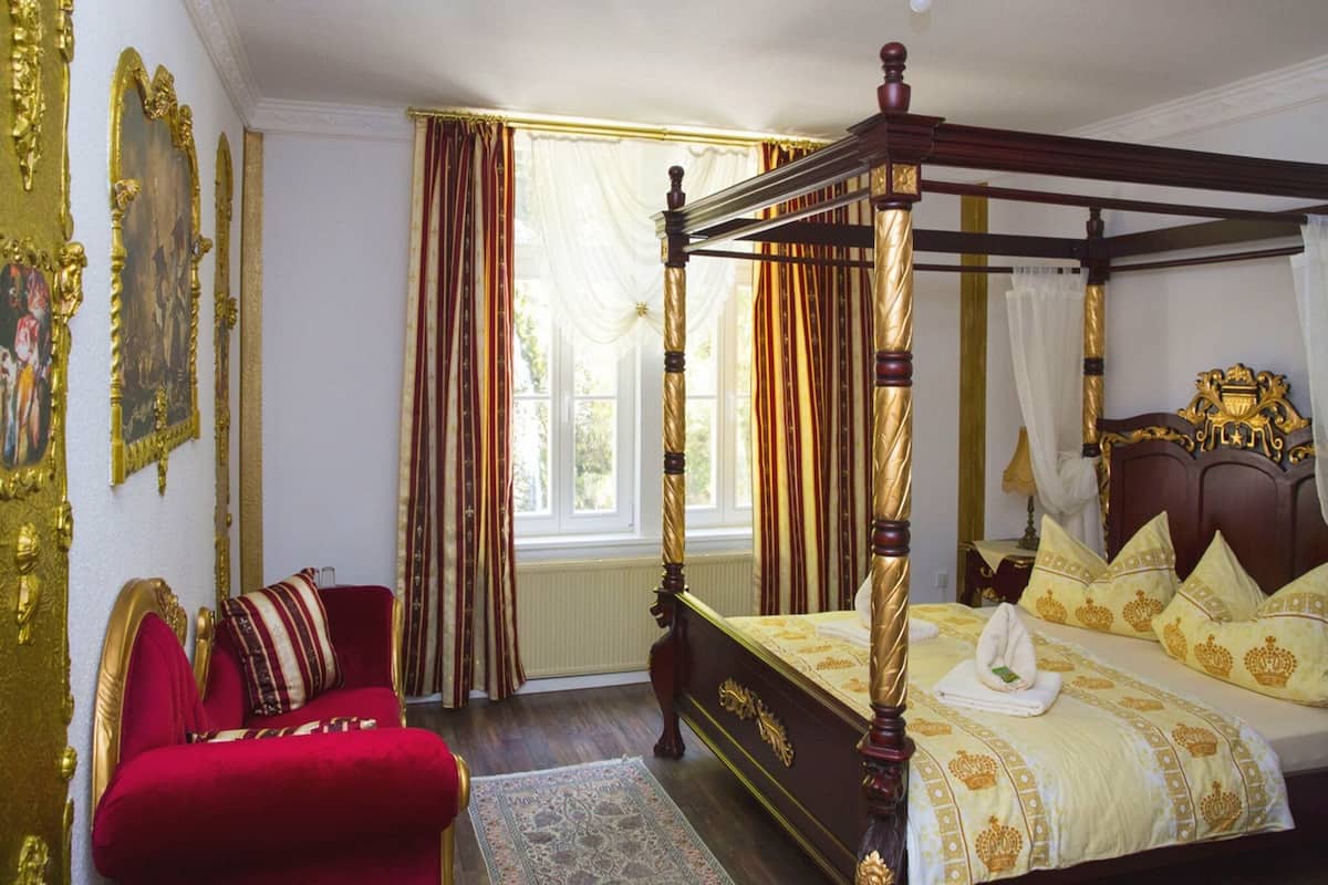 A four-poster bed with a canopy, a red upholstered chair, and ornate wall decorations.