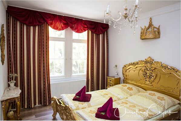 A luxurious bedroom with a large bed, ornate gold headboard, and red curtains.