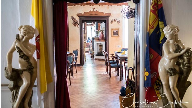 Un pasillo con piso de madera, una cortina roja y dos estatuas a cada lado.