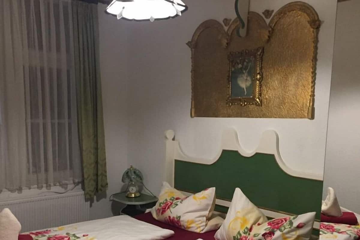 A double bed with floral bedding, a green headboard, and a decorative mirror above it.