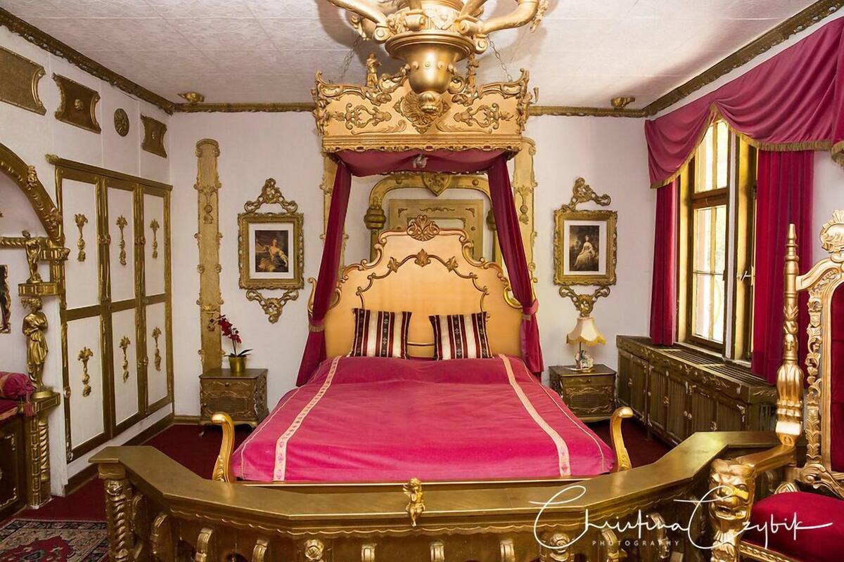 A luxurious bedroom with a large ornate bed, gold accents, and red drapery.