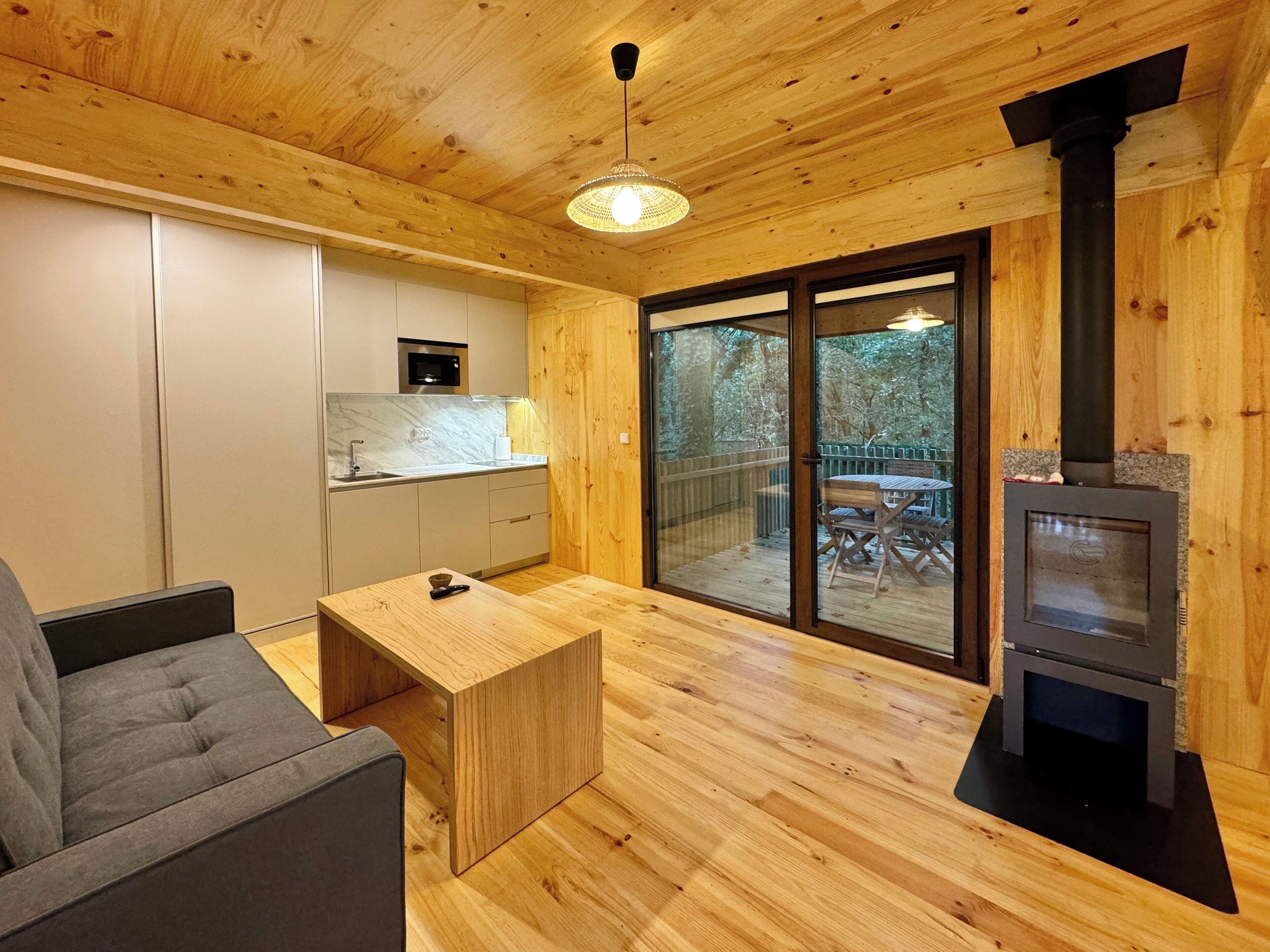 Interior moderno de cabaña con piso de madera, zona de comedor, cocina con microondas y chimenea.