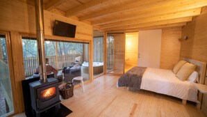 A cozy cabin with a wood-burning stove, a bed, a TV, and a patio area with a hot tub. - Enoturismo María Manuela (Boqueixon)