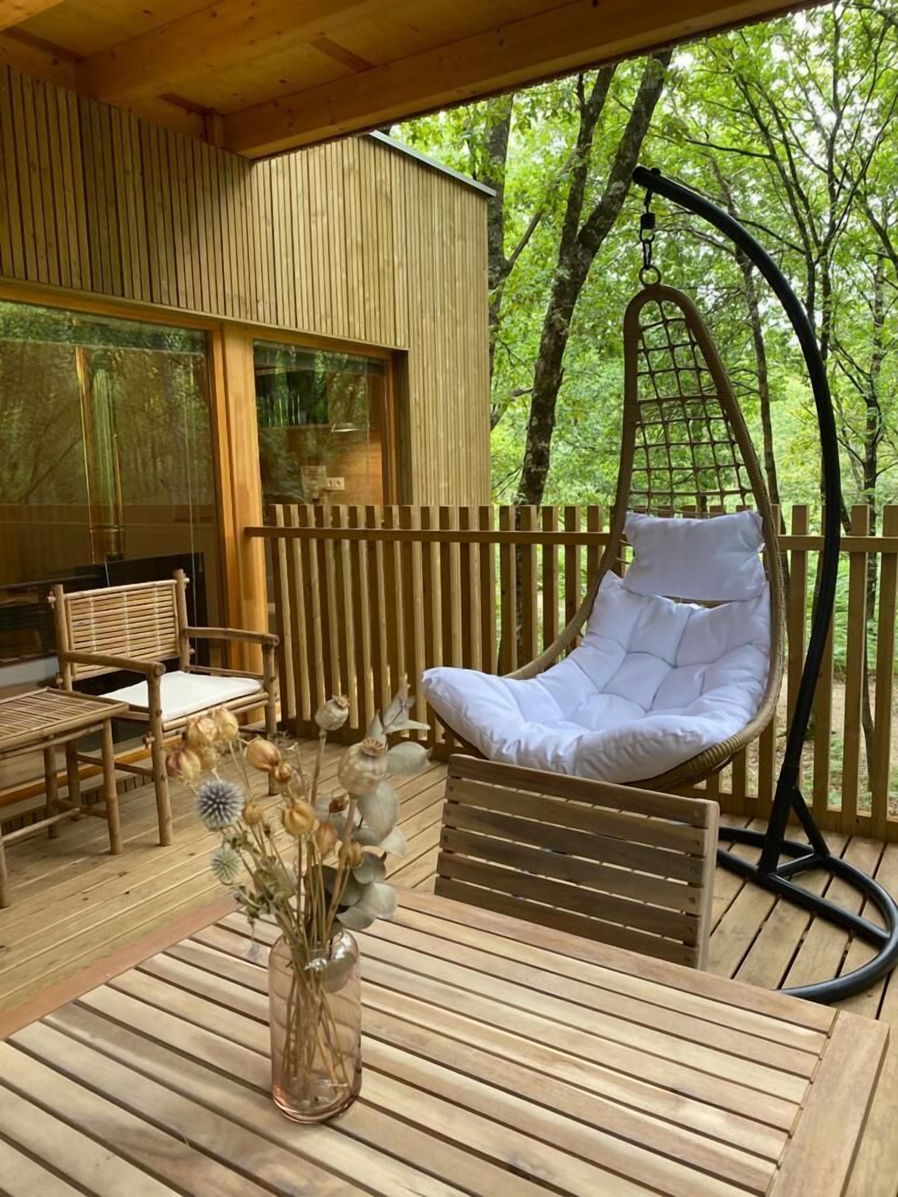 A wooden deck with a hanging chair, a table, and a vase with dried flowers.