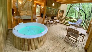 A wooden deck with a hot tub, outdoor seating, and a view of the forest. - Enoturismo María Manuela (Boqueixon)