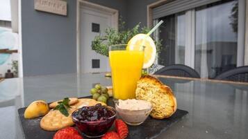 Una mesa con desayuno: tostadas, fruta, mermelada y un vaso de jugo de naranja.