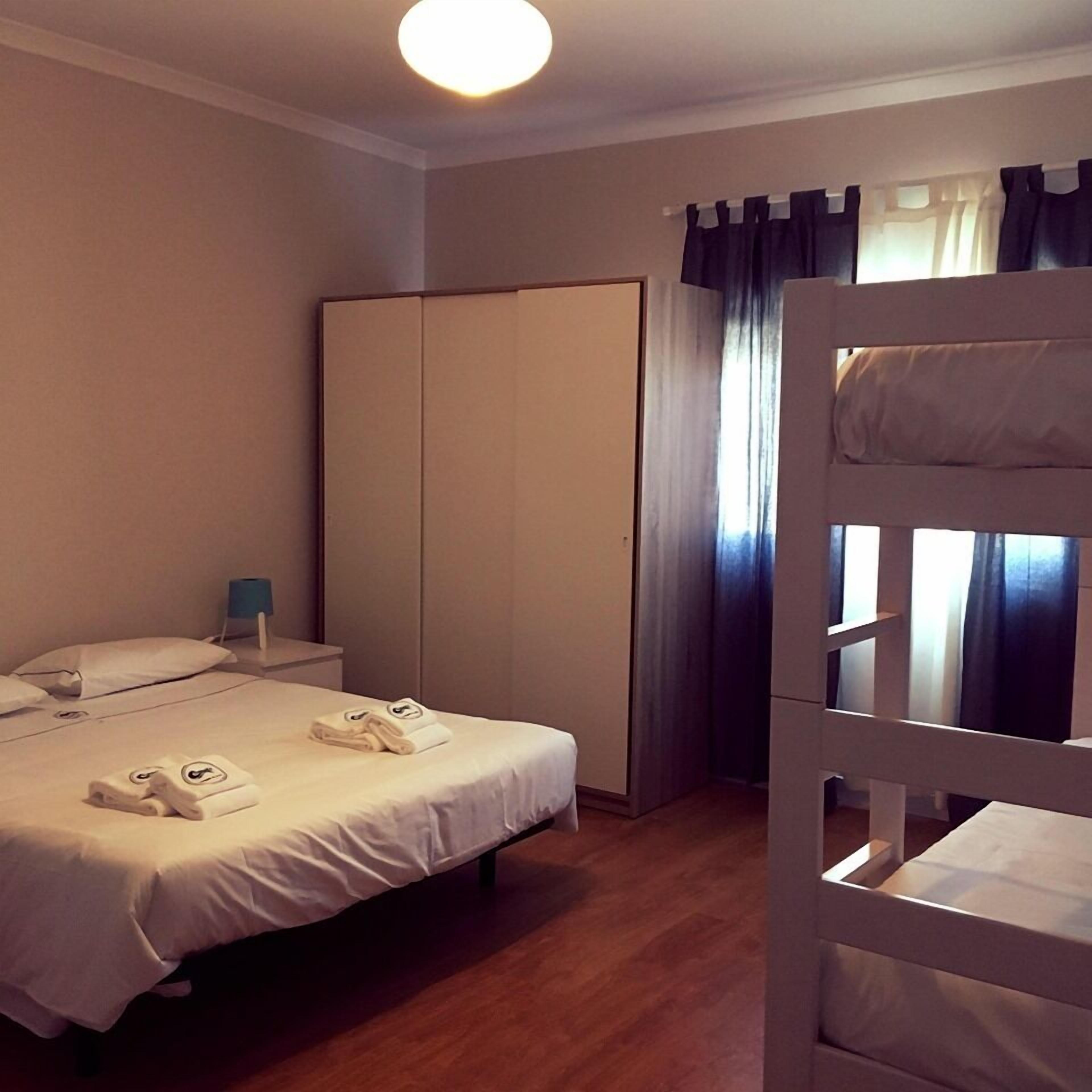A hotel room with a bed, a wardrobe, a nightstand, and a window with curtains.