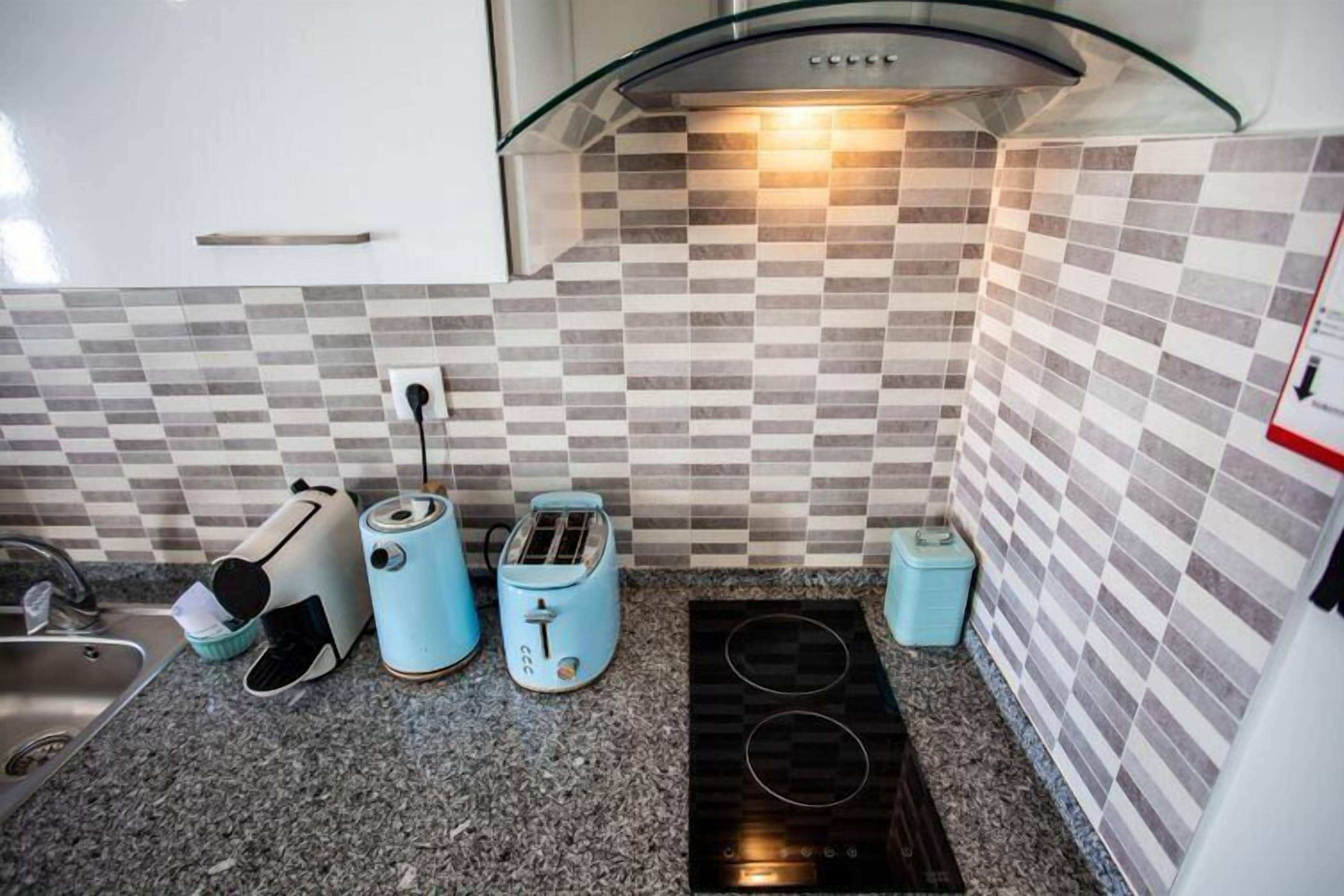 Een keuken met een zwart-wit geruit spatwand, een ingebouwde kookplaat en twee blauwe broodroosters.