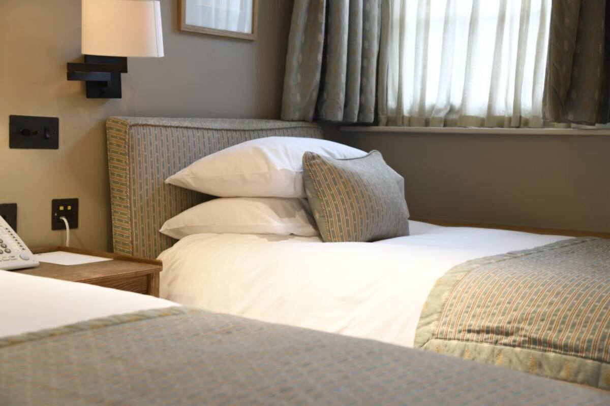 A hotel room with a bed, a bedside table with a lamp, and a window with curtains.