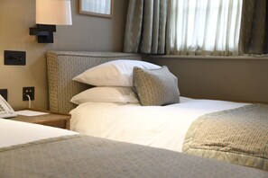 A hotel room with a bed, a bedside table with a lamp, and a window with curtains.