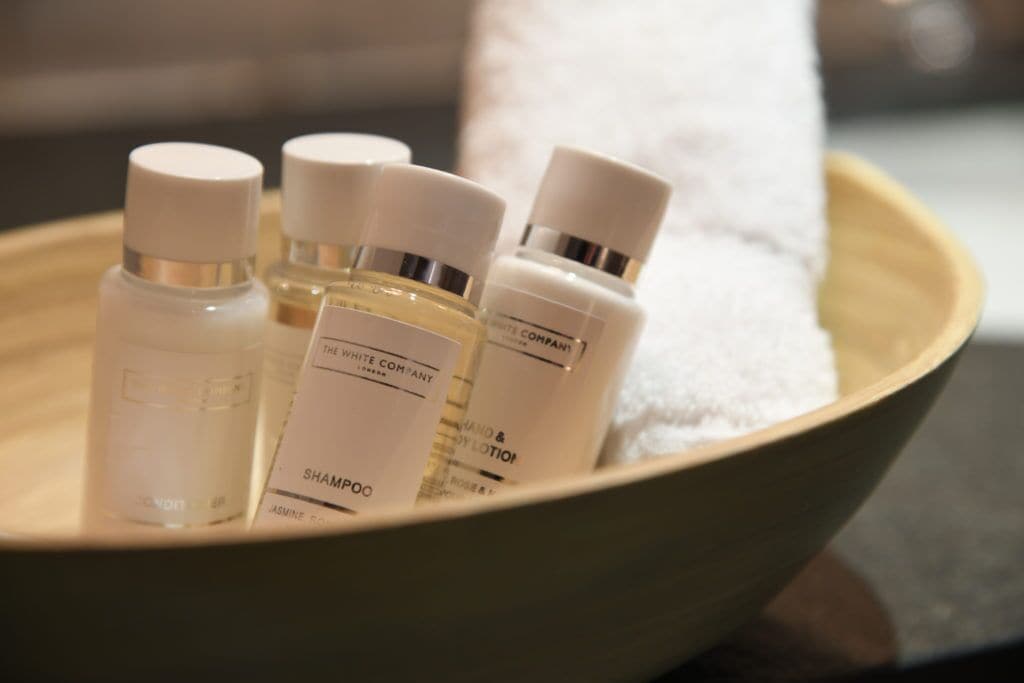 A bowl containing several bottles of toiletries, including shampoo and lotion, on a wooden surface.