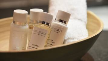 A bowl containing several bottles of toiletries, including shampoo and lotion, on a wooden surface.