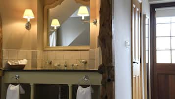 Une salle de bain avec un mur recouvert de carreaux beiges, un mur d’accent en bois, un miroir avec des appliques murales, un lavabo avec un porte-serviettes et une porte avec une fenêtre.