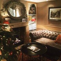 A cozy living room with a fireplace, leather sofa, and a Christmas tree.