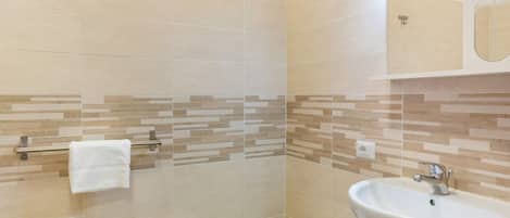 A bathroom with beige tiles, a white sink, a mirror, and a towel rack.