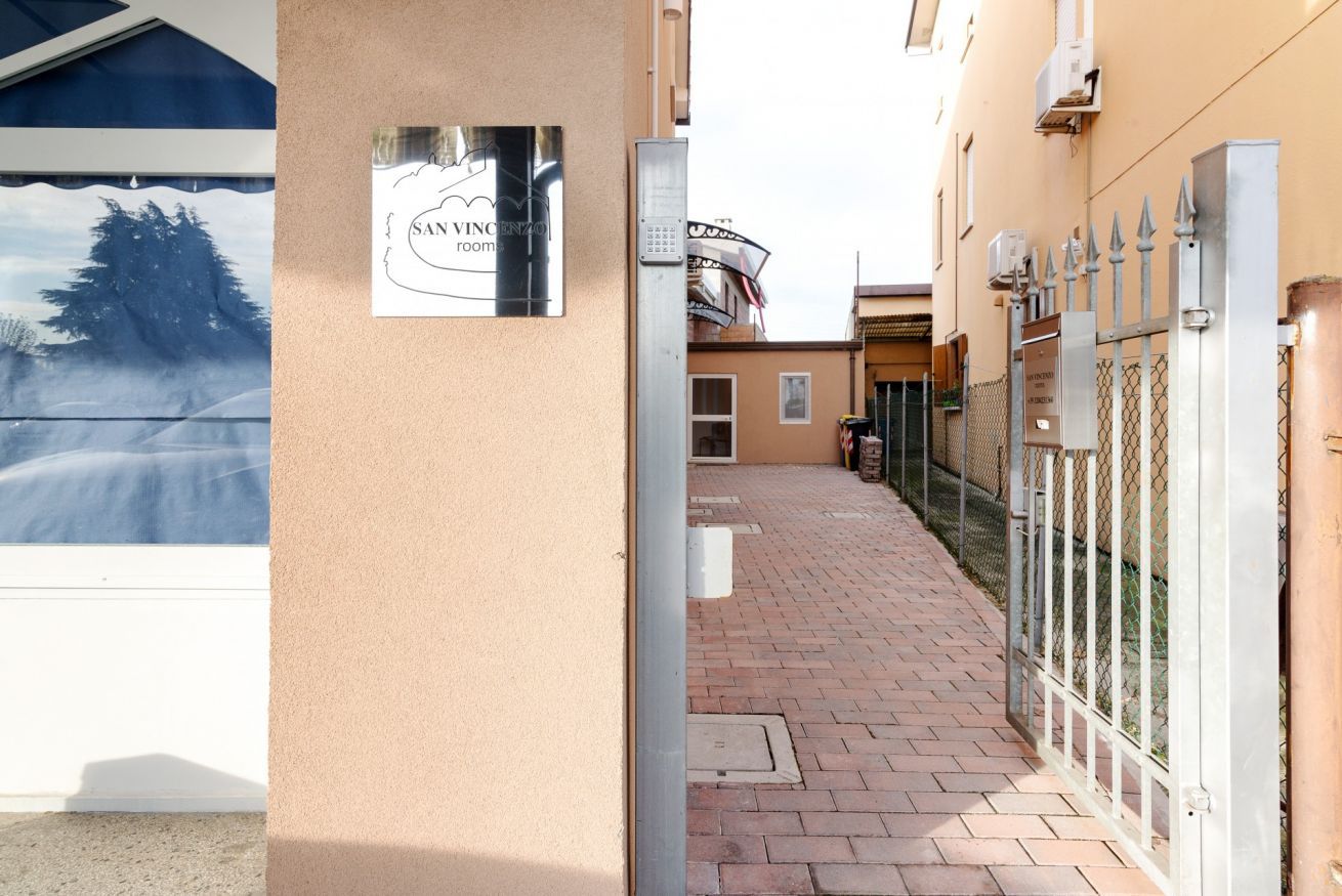 A building entrance with a sign reading 'San Vincenzo room,' a paved pathway, and a metal gate.