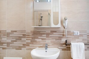 Une salle de bain équipée d’un lavabo, d’un miroir, d’une douche et d’un sèche-cheveux.