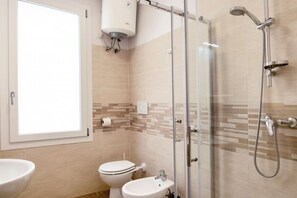 Een badkamer met toilet, bidet, wastafel, douche en een raam.