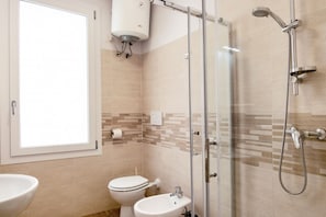 Een badkamer met toilet, bidet, wastafel, douche en een raam.