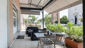 Eine Terrasse im Freien mit Tischen und Stühlen, einem überdachten Bereich und Blick auf ein Gebäude mit einem Schild.