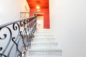 Eine Treppe mit Metallgeländern und Granitstufen führt zu einem Raum mit roter Akzentwand und einer Kristallleuchtreibe.