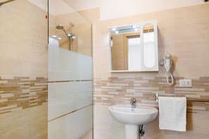 Een badkamer met een glazen douchecabine, een wastafel met spiegel en een handdoekrek.