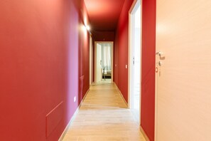 Ein Flur mit roten Wänden und Holzboden, der zu einem Zimmer mit Bett und Fenster führt.