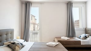 A hotel room with a bed, a smaller bed, a nightstand, and a window with curtains.