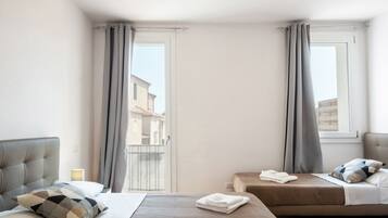 Una camera d'albergo con un letto, un letto più piccolo, un comodino e una finestra con tende.