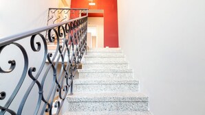 Un escalier avec des rampes en métal et des marches en granit menant à une pièce dont un mur est peint d’une couleur rouge vive et qui est agrémentée d’un lustre.