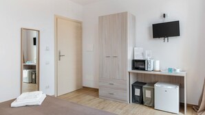 Une chambre comprenant un lit, une armoire, un bureau avec un micro-ondes, un petit réfrigérateur et un téléviseur fixé au mur.